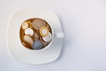 White cup of coffee with different coins on a white background. Concept of finance and business. Copy space.