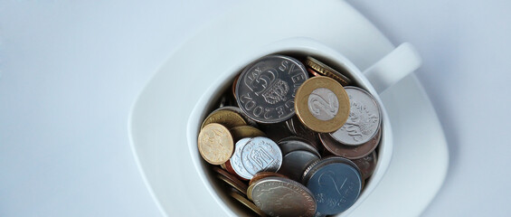 White cup of coffee with different coins on a white background. Concept of finance and business. Banner.