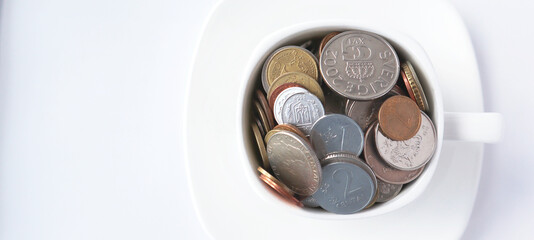 White cup of coffee with different coins on a white background. Concept of finance and business. Copy space, top view. Selective focus.