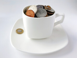 White cup of coffee with different coins on a white background. Concept of finance and business. Selective focus.