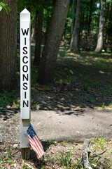 The name of the state Wisconsin engraved and painted black in a wood post painted white outside in a park