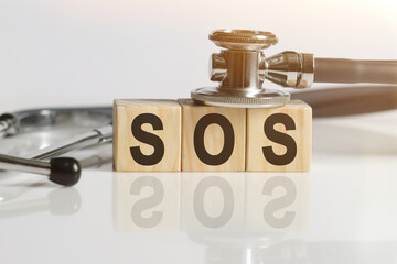 SOS the word on wooden cubes, cubes stand on a reflective white surface, on cubes - a stethoscope.