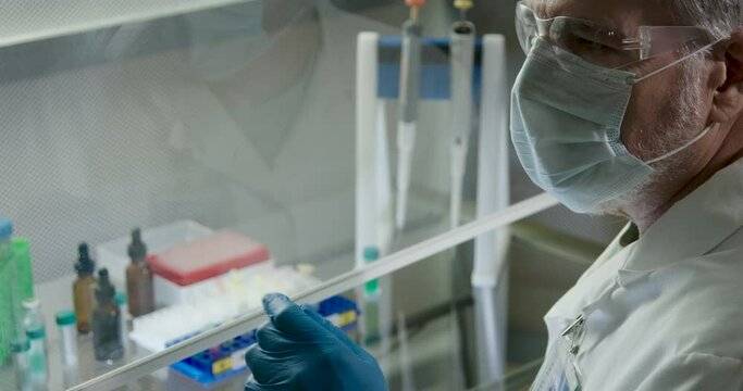 A laboratory technician checks guidelines posted off camera then proceeds with his work on pathogens behind a lab ventilation hood.