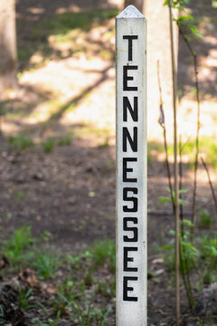 The name of the state Tennessee engraved and painted black in a wood post painted white outside in a park