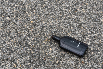 discarded empty dark brown whisky bottle with the label ripped off on a macadam sidewalk