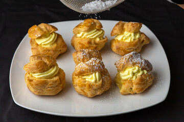 Filled creme custard pastries are being sprinkled with powdered sugar.