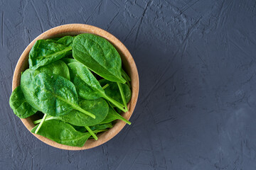 Fresh spinach leaves in wooden bowl on dark background. Organic food