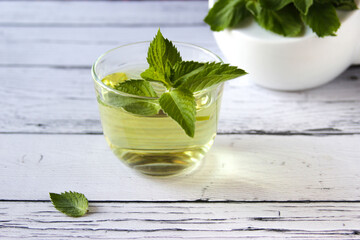 Fresh mint tea concept on a wooden background. Mint tea in a transparent cup and one mint leaf on the table