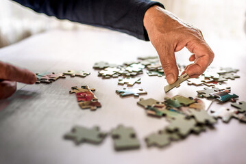 Old hand picking a jigsaw puzzle piece