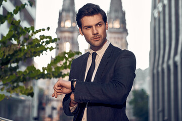 Good looking young man in full suit checking the time while standing outdoors