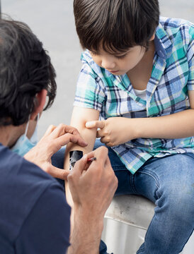 Selective Focus Kid Getting Tattoo On The Arm At A Party Event. Cropped Shot Of Process Of Applying Temporary Tattoo On Boy’s Arm. Child Having Fun Activity After Lockdown,