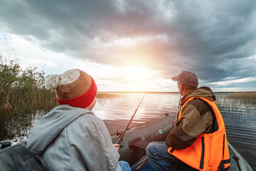 Grandson and grandfather together fish from a boat on the lake. The concept of family, summer vacation, generation. Copy space.