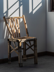 Lonely bamboo chair stands by a window with the sun shining in