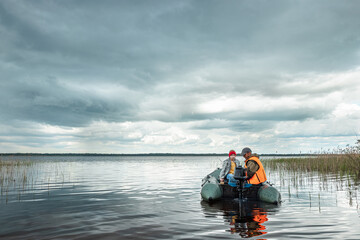Grandfather and grandson ride a motor boat on the lake. The concept of family, summer vacation, generation. Copy space.