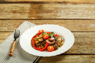 On a wooden table is a white plate of boiled mung bean with vegetables and mushrooms on a napkin and a fork. Copy space.