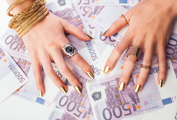 hands of rich woman with golden manicure and many jewelry rings on cash euros