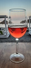 Una copa de vino tinto entre las hamacas y sombrillas de la playa al atardecer