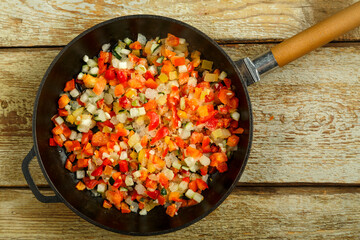 On a wooden table is a pan with frozen vegetables for cooking.