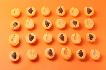 background pattern style shot of several orange ripen apricots with seeds on the bright orange color background