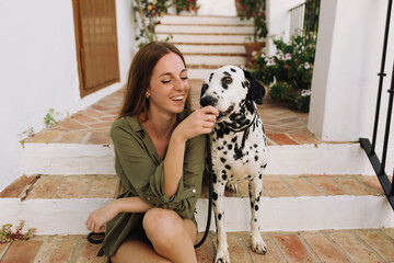 beautiful woman with long brown hair and green blouse sitting and playing with her Dalmatian dog