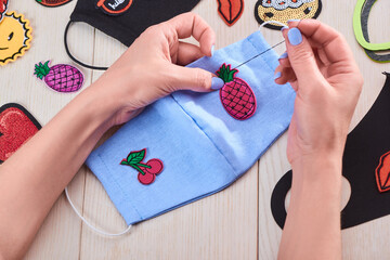 Woman sewing cute embroidered patches onto a blue face mask