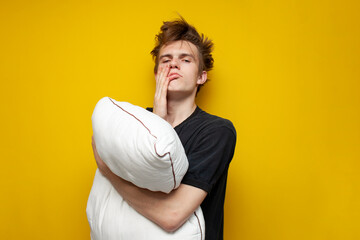 tired sleepy student with a pillow is sad on a yellow background, the guy has a problem with sleep