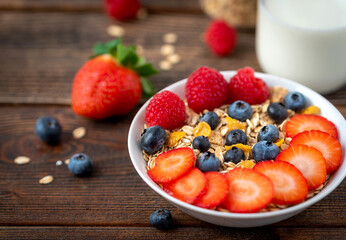 Corn flakes with blueberries and raspberries in white bowl in dark wooden desk.
