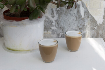 Two Glasses of coffee with cream near the leaves on white background