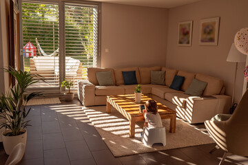 Light and shadows. Little toddler boy sit on potty playing video game on digital tablet in living room at home. Beautiful interior