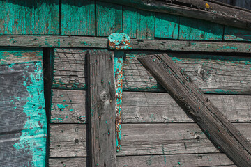 Texture, background: old gray wood with traces of green paint in bright sunlight. Old wooden house.