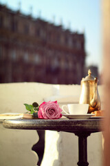 
A cup of tea on the table next to a rose and a teapot