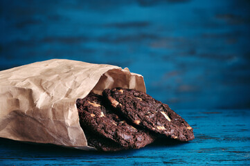Stack of chokolate cookies with cocoa, chocolate and hazelnuts on blue wooden background.