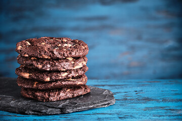Stack of chokolate cookies with cocoa, chocolate and hazelnuts on blue wooden background.