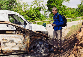 Man photographing burnt-out car on parking