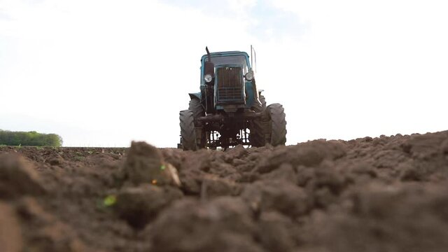 Old tractor plowing field, preparing land for sowing, driving over the camera at sunset, bottom view