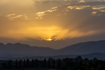 Yellow summer sunset with the sun and its rays between clouds and mountains