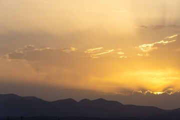 Yellow summer sunset with the sun and its rays between clouds and mountains