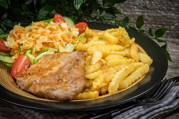 Fried pork chop in breadcrumbs, served with fries and salad.