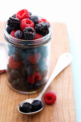 Jar full of raspberries, blackberries and blueberries on cutting board