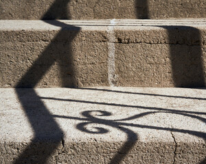 Textured coquina steps have an abstract image on them cast from the shadow of a wrought iron...