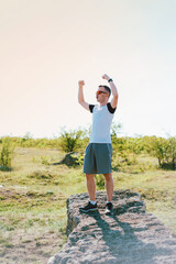 Happy young man is making the winner gesturewith both arms on a rock in field.