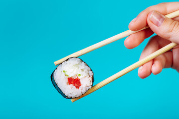Tasty sushi roll maki with wooden chopsticks on blue background close up. Place for caption and text