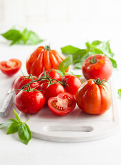 Assorted fresh ripe tomatoes and basil on white board. Healthy food concept. Clean eating