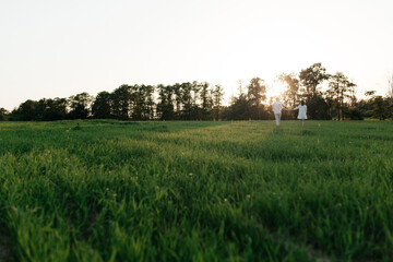 Fototapeta na wymiar Happy young couple walking on the field with green grass on the sunset. Love story
