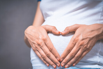 Pregnant Woman holding her hands in a heart shape on her baby bump. Pregnant Belly with fingers Heart symbol. Maternity concept. Toned photo of pregnancy.