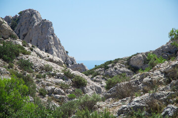 Fototapeta na wymiar Landscape of mountaint with small rocks and green bushes under the blue sky with the sea in the background in the Calanques de Marseille in France