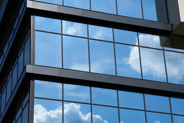 facade of a modern building on a bright Sunny day, blue sky and clouds reflecting in a glass, beautiful exterior of the new building