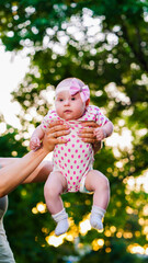 Little baby with pink headband on arms of mother on tree background
