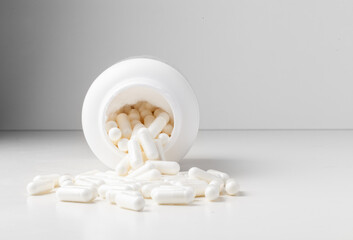 White pills spilled from a toppled white pill bottle on the white background