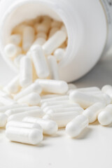 White pills spilled from a toppled white pill bottle on the white background